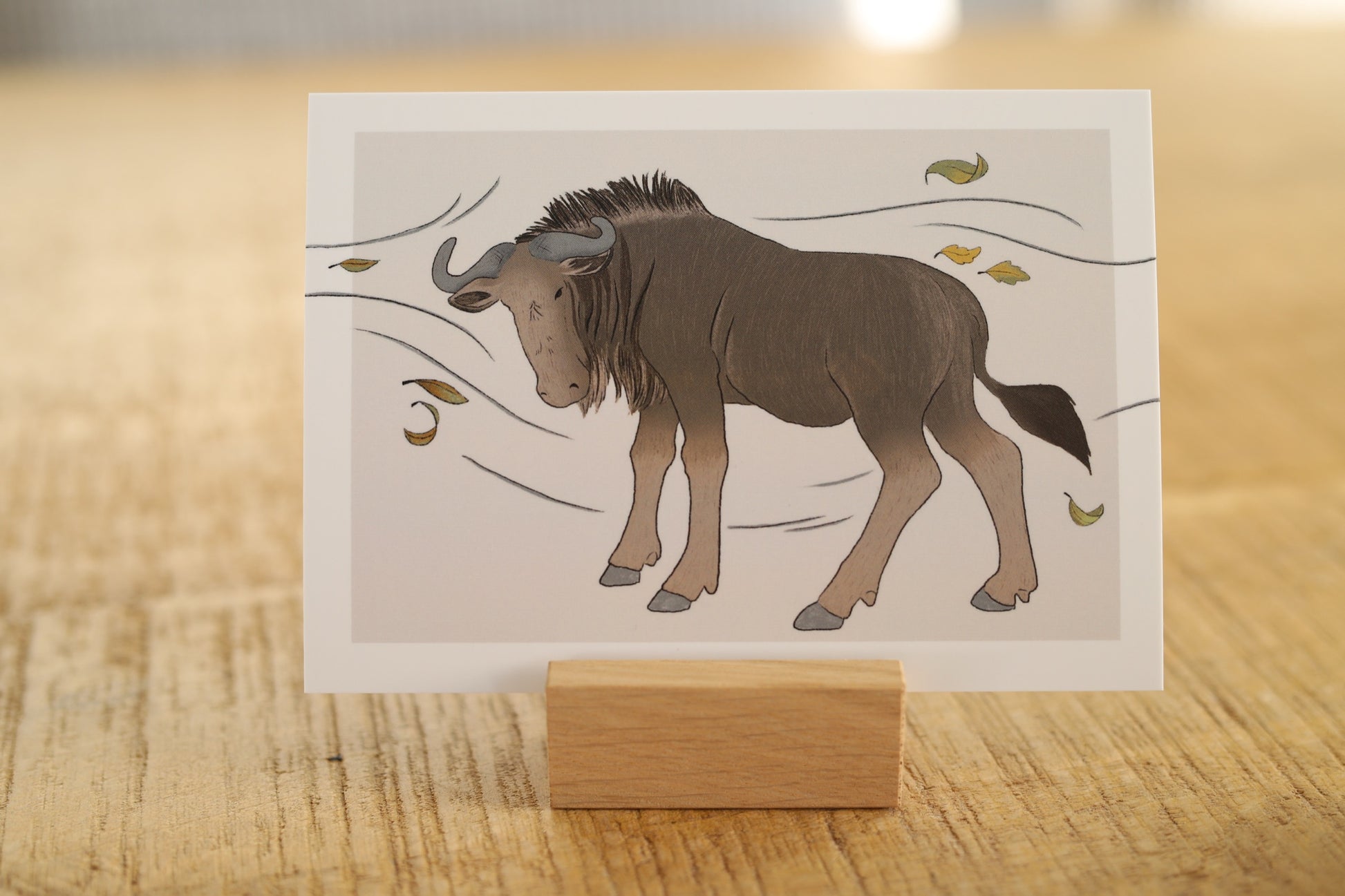 Das Foto zeigt eine Karte in einem Holzkartenhalter. Auf der Karte ist ein Gnu abgedruckt, welches in einem Sturm steht.